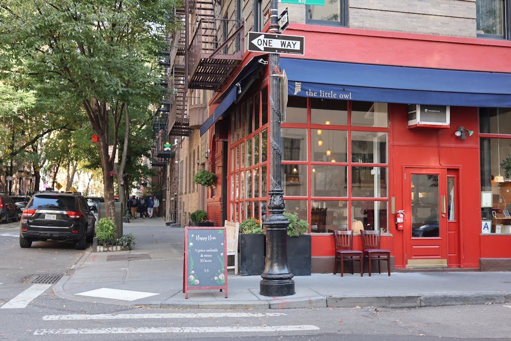 Cozy corner cafe and city street scene in New York with vibrant red facade and sidewalk seating.