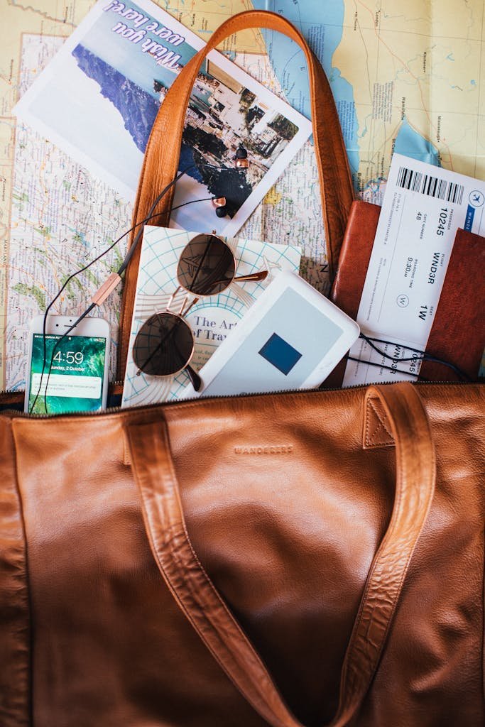 Flat lay of travel essentials including a leather bag, map, sunglasses, and tickets.