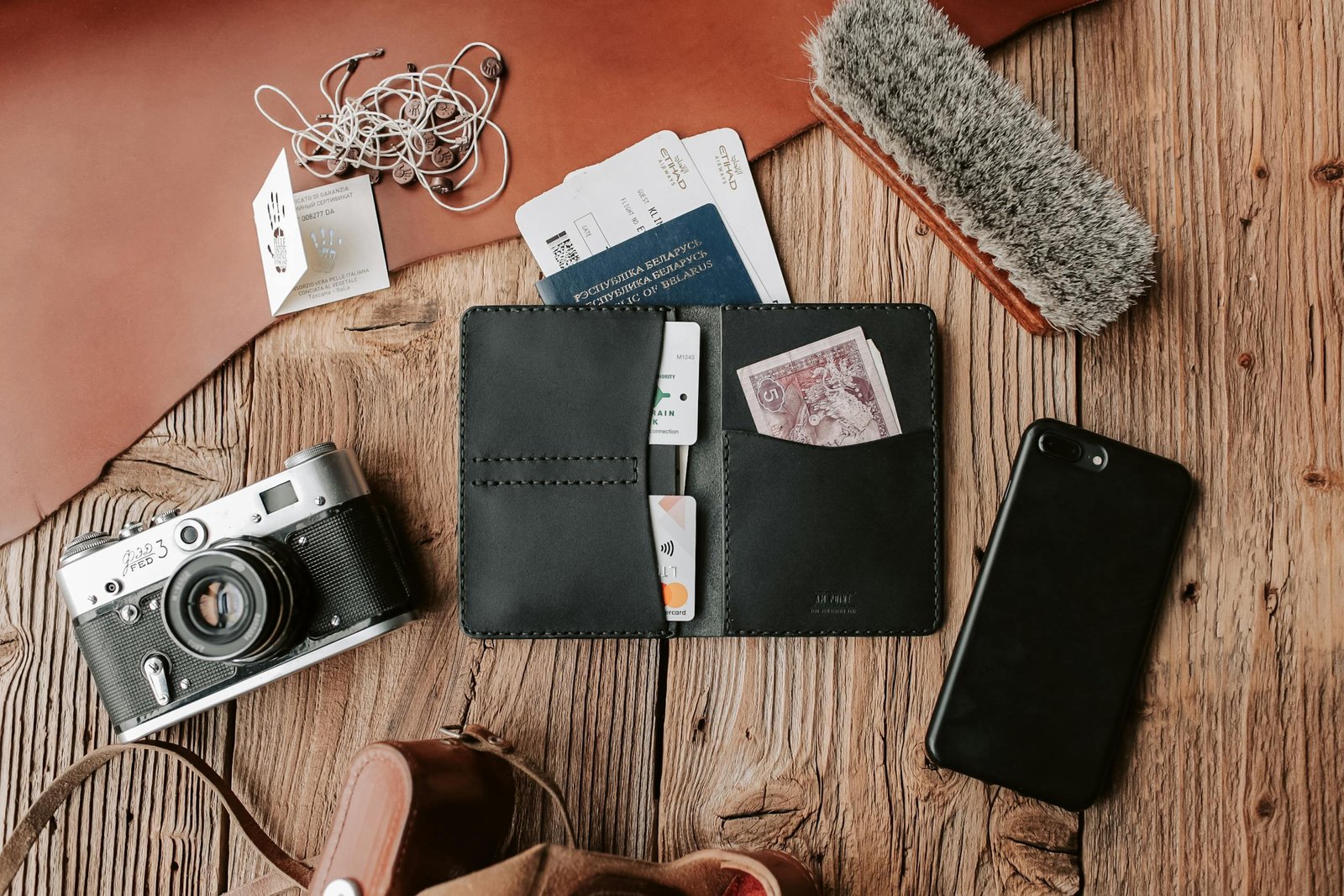 Flat lay of traveler essentials including passport, boarding pass, camera, and phone on wooden surface