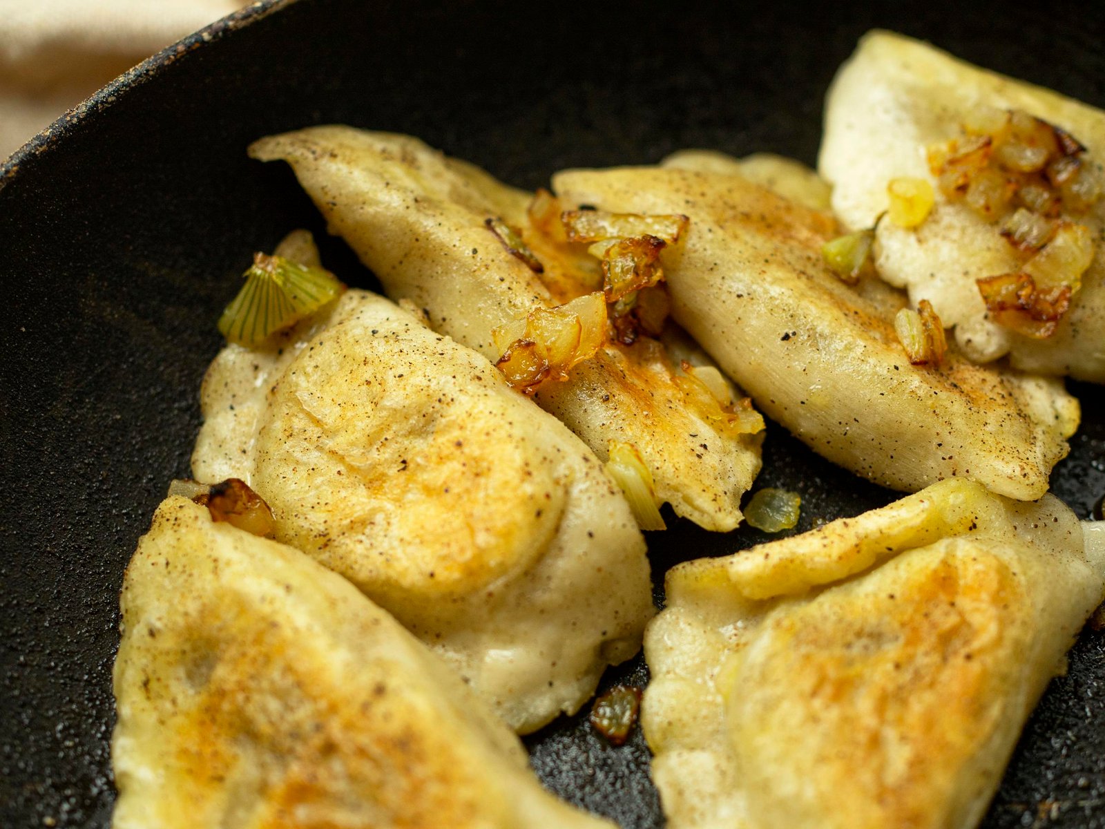 Appetizing fried dumplings with onions in a frying pan, showcasing traditional cuisine.