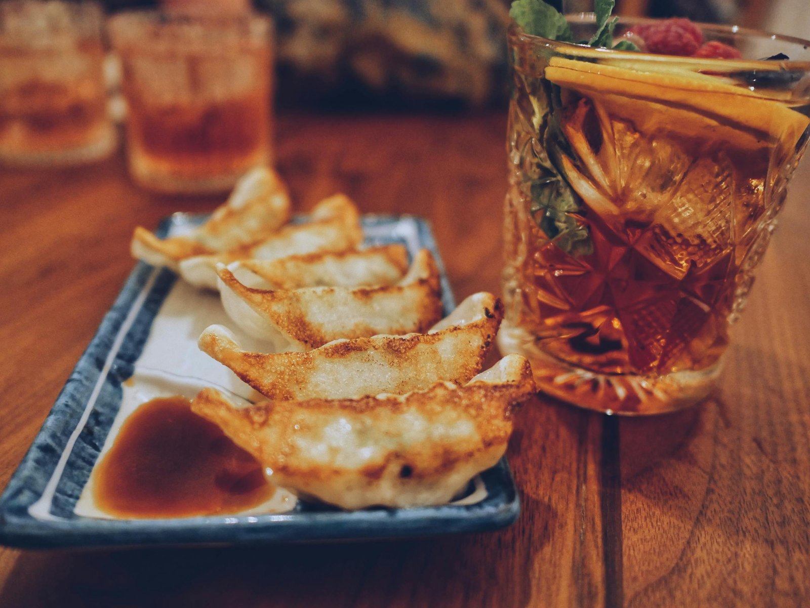 Close-up of fried dumplings with dipping sauce and a glass of iced beverage on a wooden table.