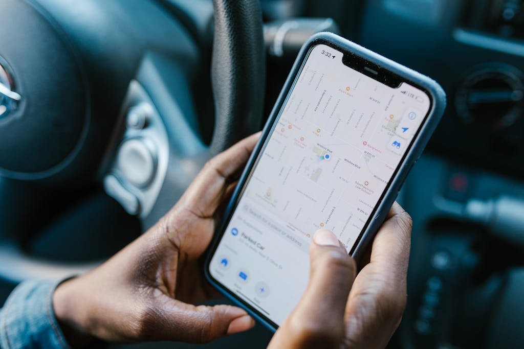 Close-up of hands holding a smartphone with GPS navigation displayed, in a car setting.