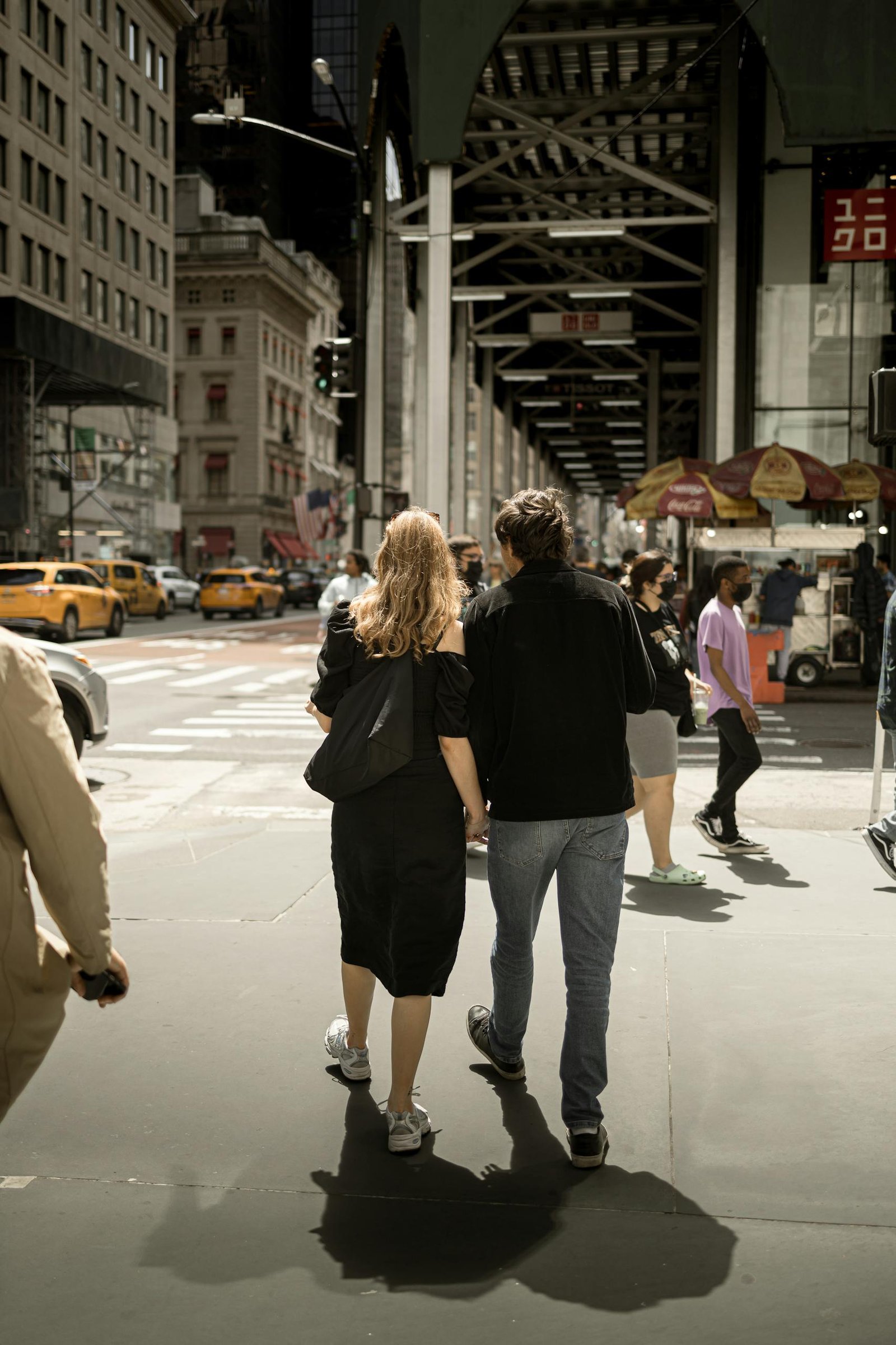 A couple walks hand in hand on a busy New York City street, surrounded by iconic yellow cabs.