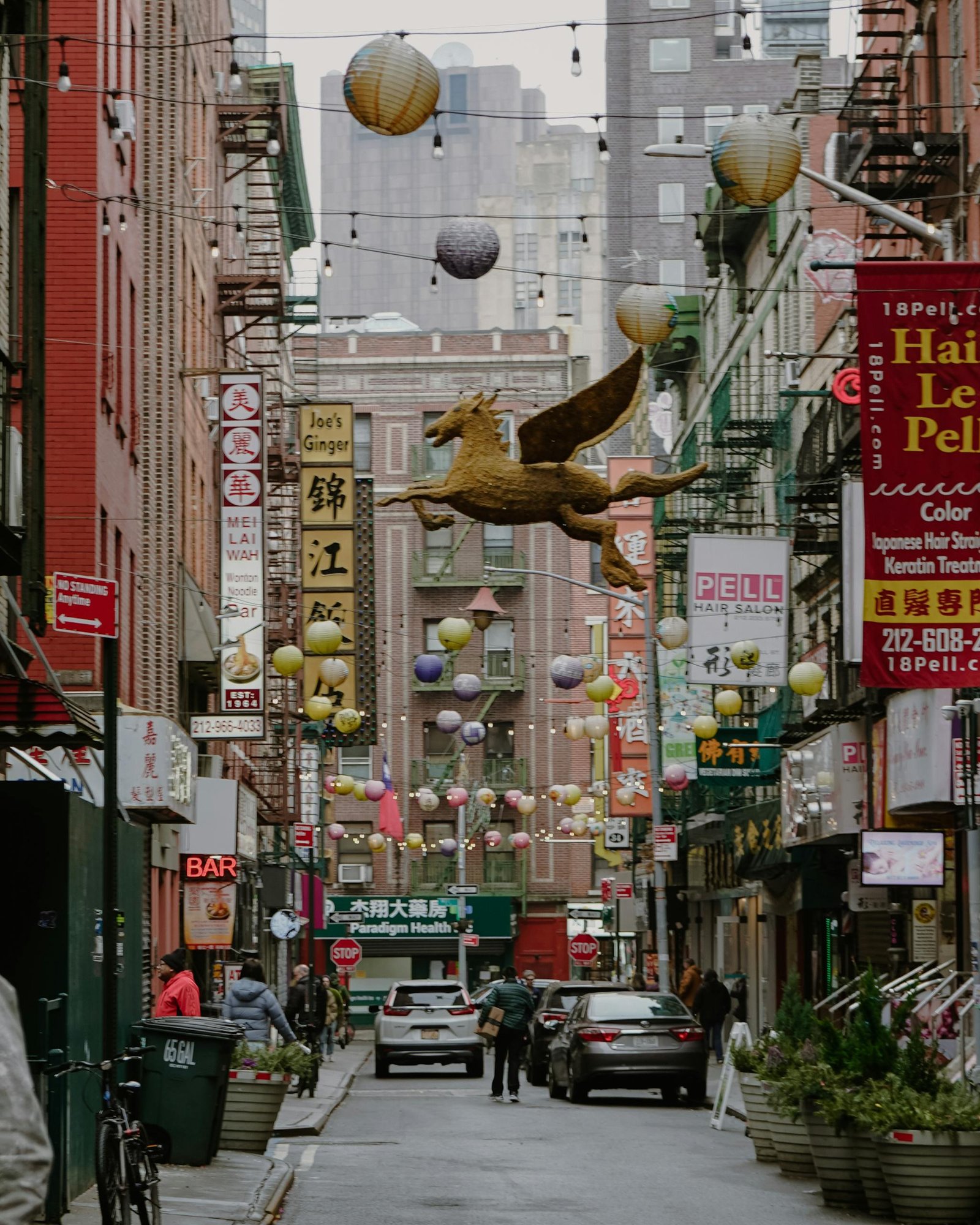 A lively urban scene in Chinatown, New York City featuring lanterns, signs, and a Pegasus sculpture.