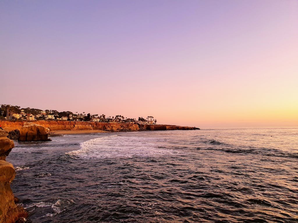 A tranquil sunset view of the San Diego coastline with calm waves and vibrant skies.