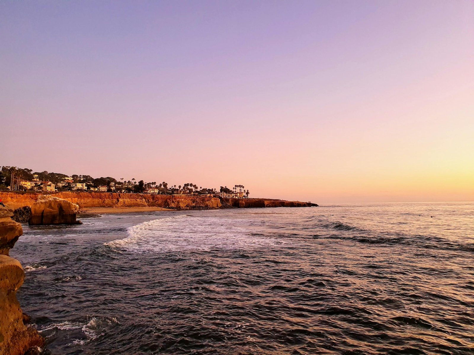 A tranquil sunset view of the San Diego coastline with calm waves and vibrant skies.