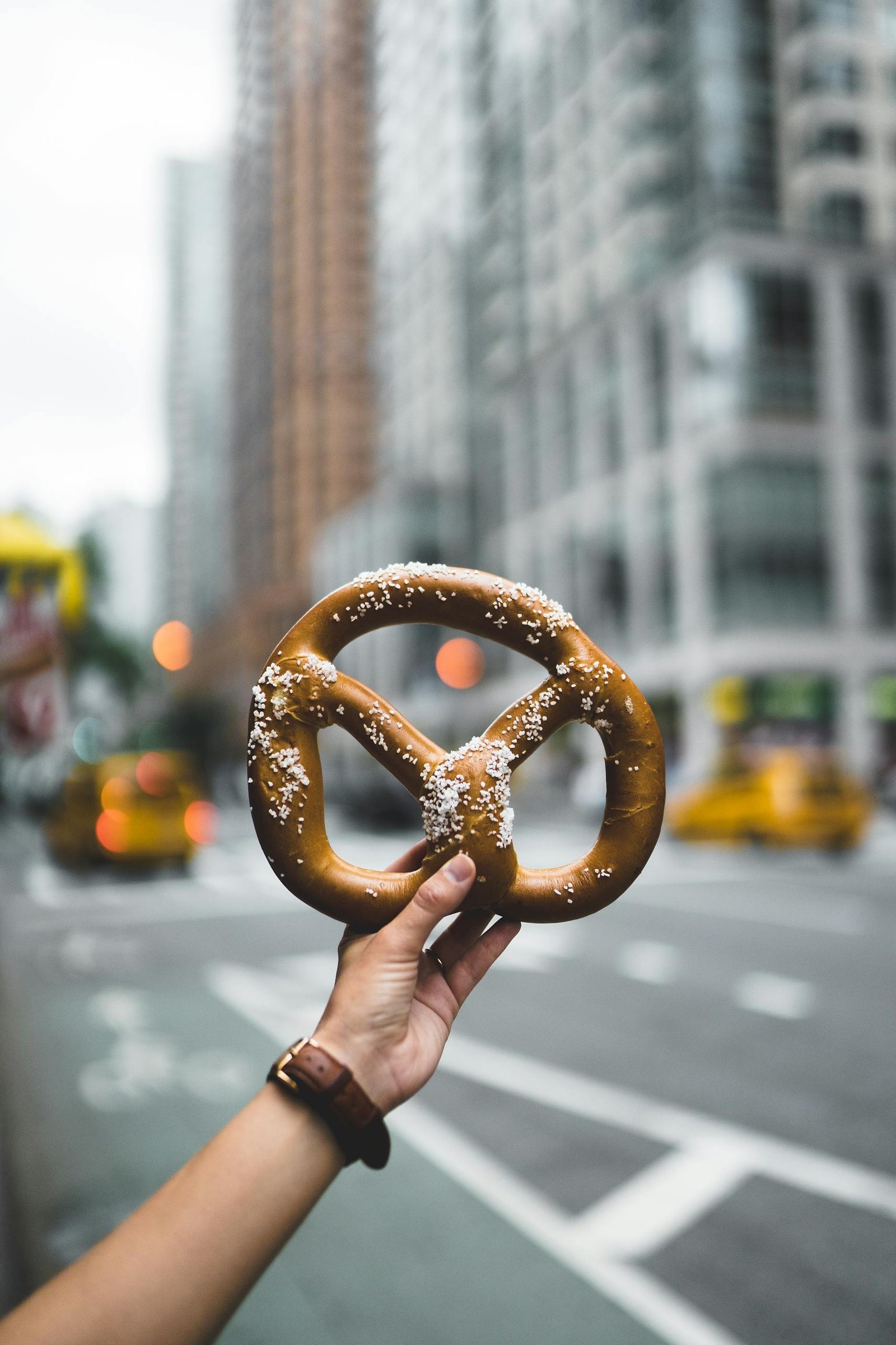 Close-up of a hand holding a salted pretzel against a bustling New York City street backdrop.