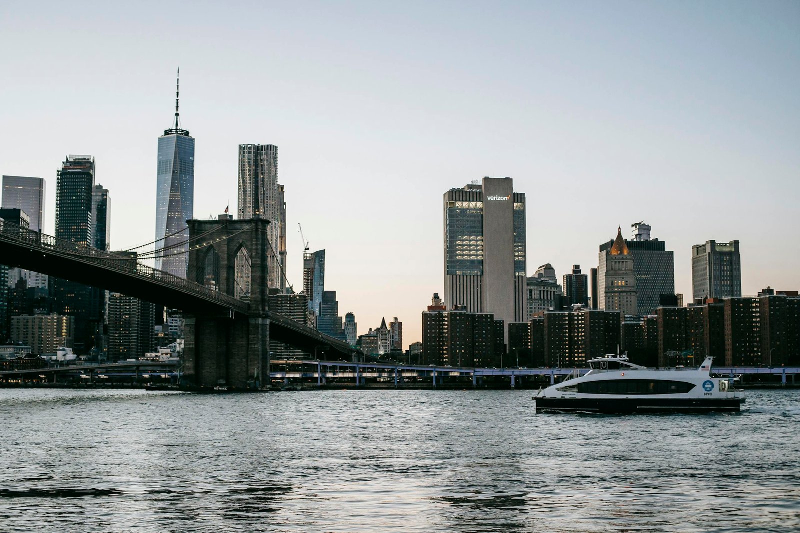 Scenic view from the NYC ferry boat of Brooklyn Bridge and NYC skyline with boats in the river during twilight.