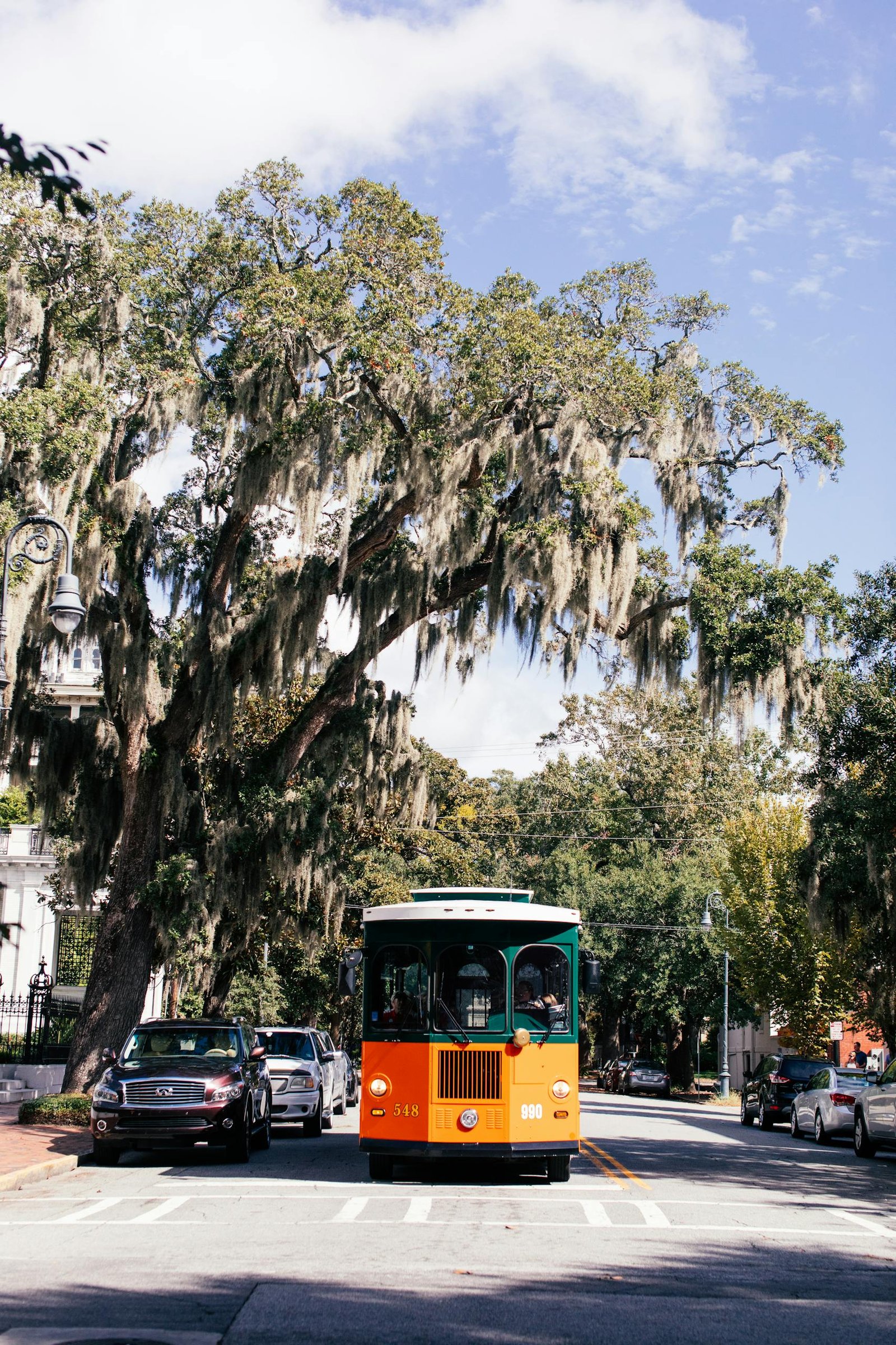 Vintage trolley on a scenic street in Savannah, Georgia surrounded by lush trees.